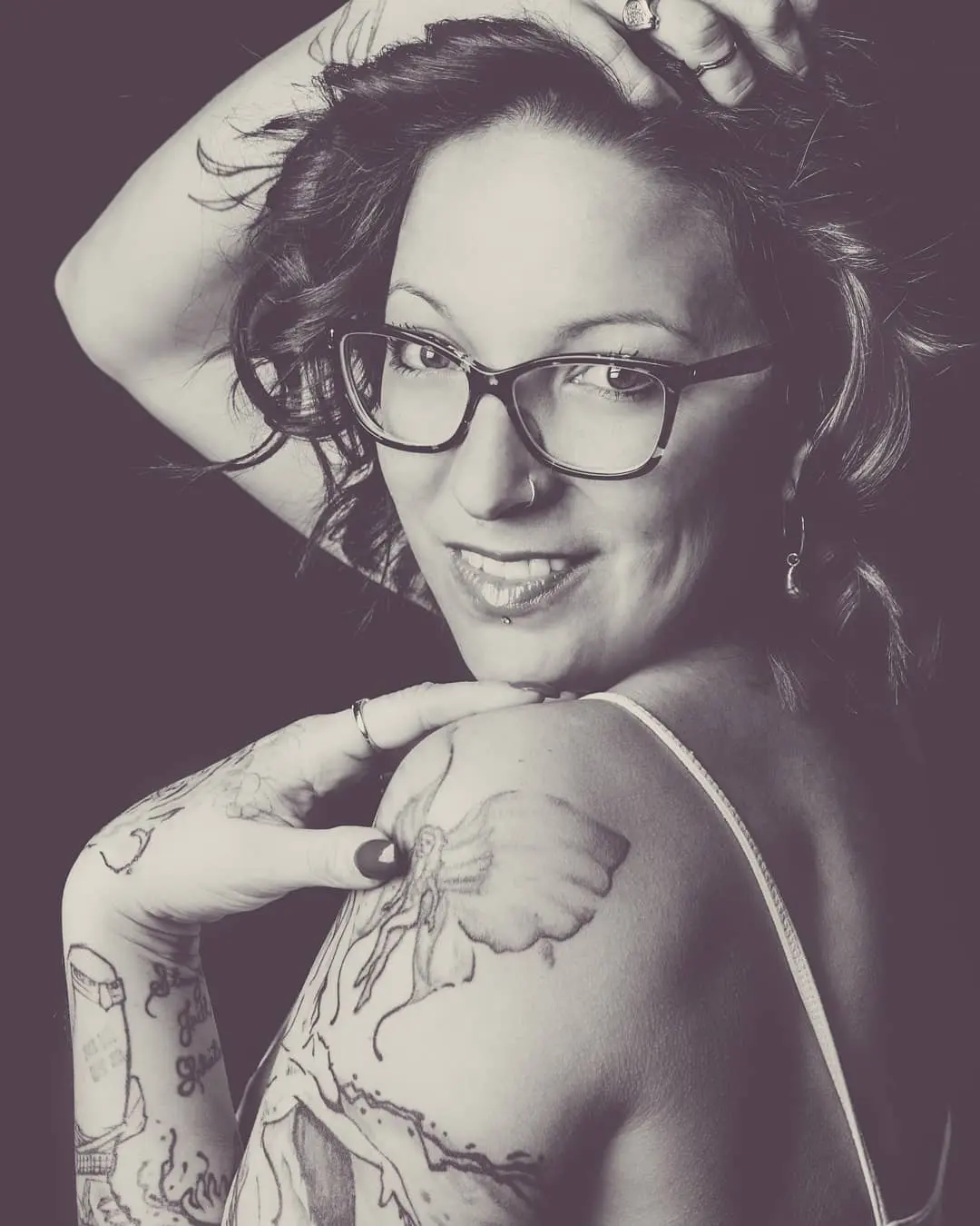 A woman with glasses and tattoos on her arms.